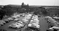 VIEW WEST LOOKING DOWN AND ACROSS CROWDED PARKING LOT FULL OF AUTOS FROM VERKAMPS ROOF TOWARDS THE EL TOVAR HOTEL & HOPI HOUSE. JULY 1951.  NPS PHOTO BY DAZEY