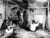NATIVE ARTISANS DEMONSTRATE AT HOPI HOUSE SHOP. BASKET & RUG WEAVERS. MAN SMOKING. CIRCA 1910. FRED HARVEY CO.  GRCA 15803E