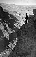 TRANS-CANYON TELEPHONE LINE CONSTRUCTION -  SILOUETTE OF CCC ENROLLEE ATTACHING WIRE TO POLE AT THE EDGE OF A STEEP CLIFF NEAR THE RIM. INNER CANYON BEYOND. CIRCA 1935. NPS PHOTO BY LAWS  <br><br>