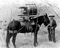 ERNIE W. ENSOR, NPS MAINTENANCE, WITH A WASHING MACHINE PACKED ON BACK OF MULE, RASTUS. THE MACHINE WAS TAKEN DOWN THE BRIGHT ANGEL TRAIL FOR USE AT PHANTOM RANCH. JAN 1939. NPS, ENSOR. 