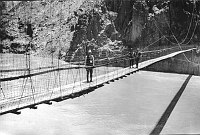3 MEN CROSSING FIRST (1921) SWINGING SPENSION BRIDGE OVER COLORADO RIVER. WAS LOCATED BELOW THE PRESENT BLACK BRIDGE.  CIRCA 1927. NPS, MATTHIS. 