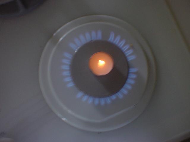 A lit candle in the middle of a burner on my stove that looks like a flower of fire.