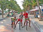 the act of the 3 young boys on their sporty vehicle on the walking lane parellel to the beach.
